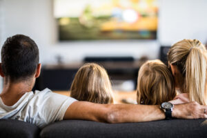 Rear view of a family watching TV on sofa at home.