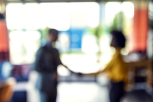 Blurred figure of a man and woman shaking hands in an office building.