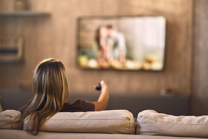 Back view of relaxed woman watching TV at home