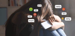 Girl with head on her knees holding phone. Emojis and mean words like nasty, gross, stupid on image