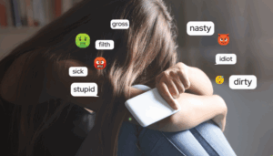 Girl with head on her knees holding phone. Emojis and mean words like nasty, gross, stupid on image